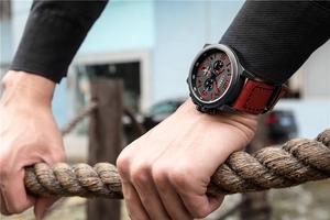 Men's sports watch with black case and red leather strap worn during outdoor activities