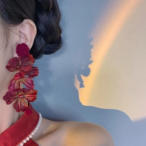 Detail of red rose earrings with layered petals and long pendant on model with sunlight