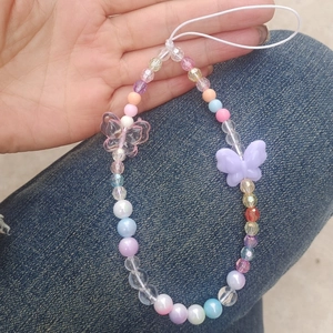 Detail of beaded phone strap with pink and purple butterfly charms held in hand