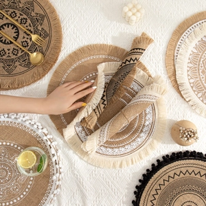 Nordic handmade round jute placemat with mandala print and tassels on a textured white surface