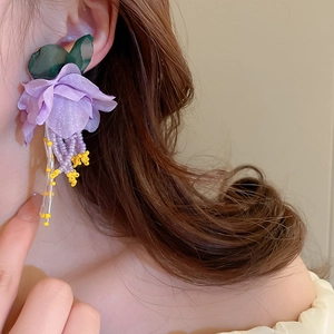 Detail of purple fabric flower earrings with beaded tassels worn by a model