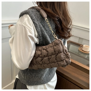 Détail d'un sac nuage matelassé marron foncé avec chaîne dorée porté par un modèle