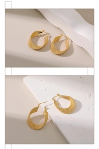Close-up detail of 18K gold plated braided texture hoop earrings on white geometric blocks