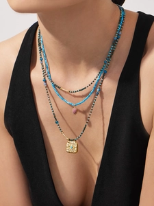 Detail view of multi-layer turquoise bead necklace with evil eye coin and pink stone pendant