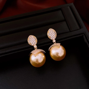 Detailed macro view of 18k gold-plated pearl earrings with sparkling zircon leaf accents