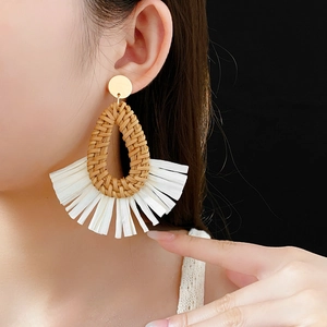 Detail of hand-woven brown raffia fan-shaped earrings with dense white tassels on a model