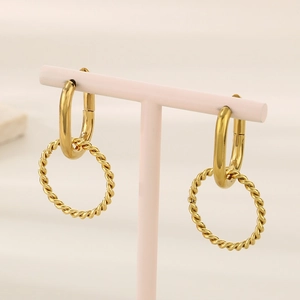 Detailed close-up of golden twisted hoop earrings on a light pink display stand