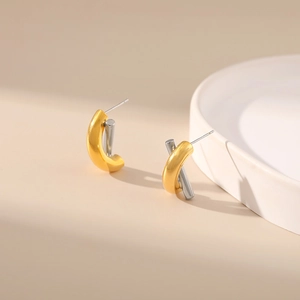 Close-up of bicolor gold and silver twisted earrings on an elegant beige background