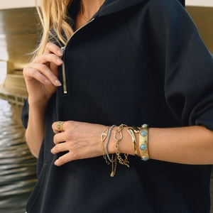 Evil eye OT buckle bracelet and gold plated bangle set worn by a model near water