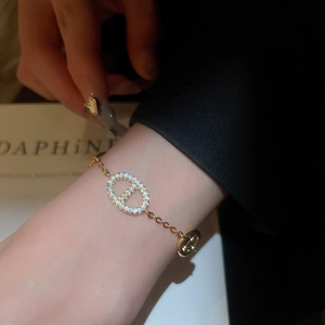 Detail shot of a gold-plated bracelet with a zircon-encrusted oval charm on a female wrist
