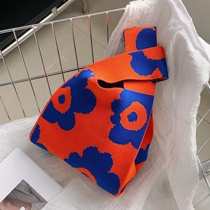 Detail of orange knitted tote bag with blue floral pattern on textured fabric