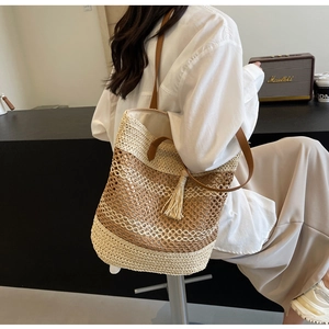 Detail of woven straw bucket bag with brown leather straps and fringe tassel charm