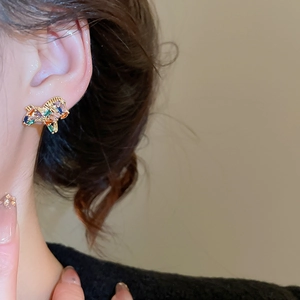 Close-up of colorful crystal animal stud earrings with gold plating on a model's ear