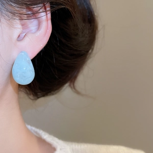Macro shot of elegant light blue resin teardrop earrings worn by a model in soft lighting