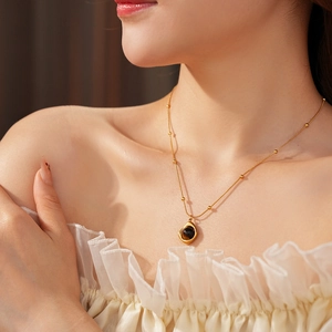 Detail of tiger eye stone pendant on gold bead chain necklace worn by model