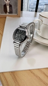 Detail of silver metal strap and black square dial watch on a wooden table setup