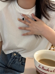 Close-up of a silver S925 necklace with black oval pendant and matching minimal ring on a model