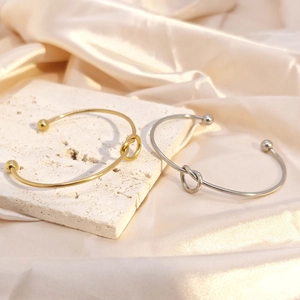 Minimalist knot open bracelets in gold and silver finish on elegant silk background