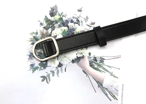 Close-up of black faux leather belt with a light gold D-ring buckle on fashion magazine