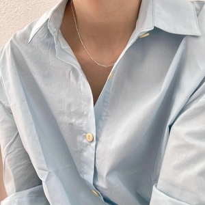 Close-up of minimalist silver twisted chain necklace worn with a light blue shirt
