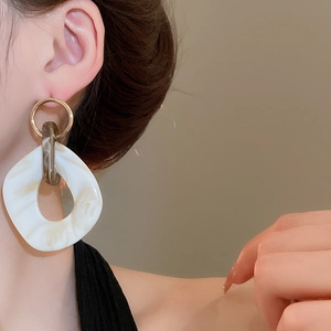 Close-up of golden irregular oval hoop earrings with white marble resin pendant on model