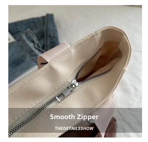 Detail of silver metal zipper closure on canvas tote bag with pink webbing handles