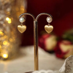 Dettaglio macro di orecchini a cuore in oro con perle bianche su un supporto