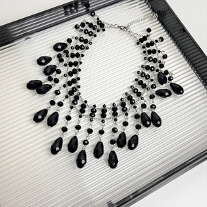 Detail of layered black beaded necklace with silver chain and a dark teardrop pendant