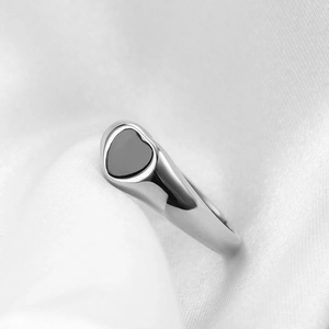 Macro view of silver heart ring with black shell inlay on a soft white silk fabric