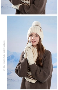 Close-up of off-white knitted winter set featuring warm pompom beanie, scarf and gloves