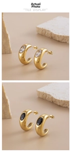 Detail view of C-shaped gold earrings with large oval white and black zircon gemstones