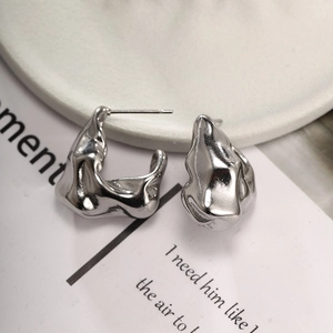 Detail of silver irregular lava texture earrings on white ceramic and card