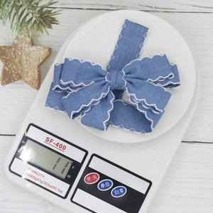 Detail of blue denim bow hair clip with white wavy embroidered edges showing fabric texture