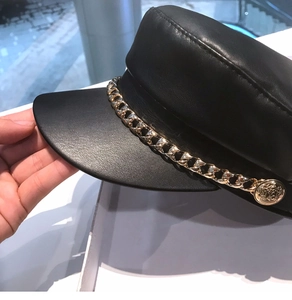 Detail of black leather newsboy cap featuring a golden chain and lion crest buckle