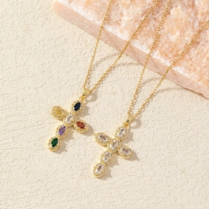 Gold plated cross necklaces with multicolored and white zircons on a beige stone surface