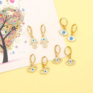 Détail de quatre boucles d'oreilles dorées avec œil maléfique et main de Hamsa en émail