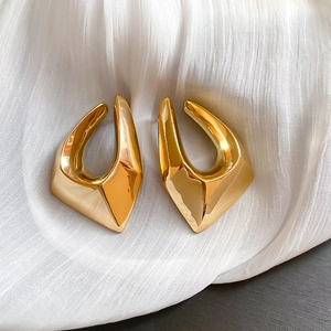 Détail macro de boucles d'oreilles dorées géométriques avec surface 3D sur tissu blanc