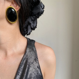 Close-up of vintage gold-rimmed oval black earrings on model with retro aesthetic