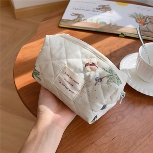 Close-up of beige quilted cotton makeup bag with cute rabbit print held by hand