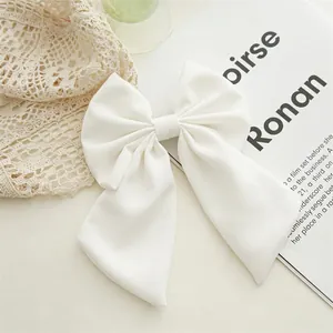 Detail of elegant large white fabric bow hair clip with long ribbons on soft background