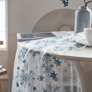 White sheer Christmas tablecloth with blue and gold snowflakes on a round table