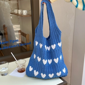 Detail of navy knit tote bag with white heart patterns held by a model in a cafe