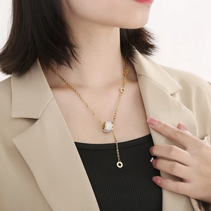 Detail of gold titanium steel necklace featuring a cat-eye cylinder pendant on a model