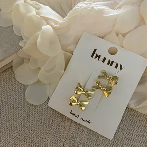Detailed view of four golden bow-shaped metal hair clips on an elegant cream display card