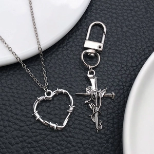 Silberne Dornen-Herz-Halskette und Kreuz-Rosen-Schlüsselanhänger auf schwarzem Leder