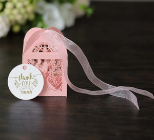 Detailed view of pink laser-cut candy box with silk ribbon and thank you tag