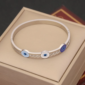 Polished silver evil eye bangle with blue enamel details in a beige jewelry box