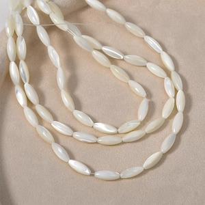 Natural white shell oval rice beads for DIY jewelry making displayed on beige velvet fabric
