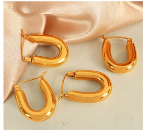 Close-up of polished gold U-shaped hoop earrings on elegant silk and leather texture