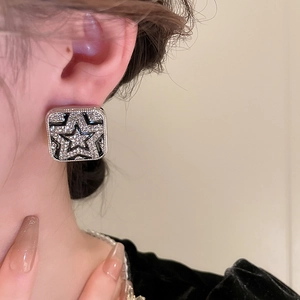 Close-up of a square stud earring with a diamond-studded star and black enamel finish
